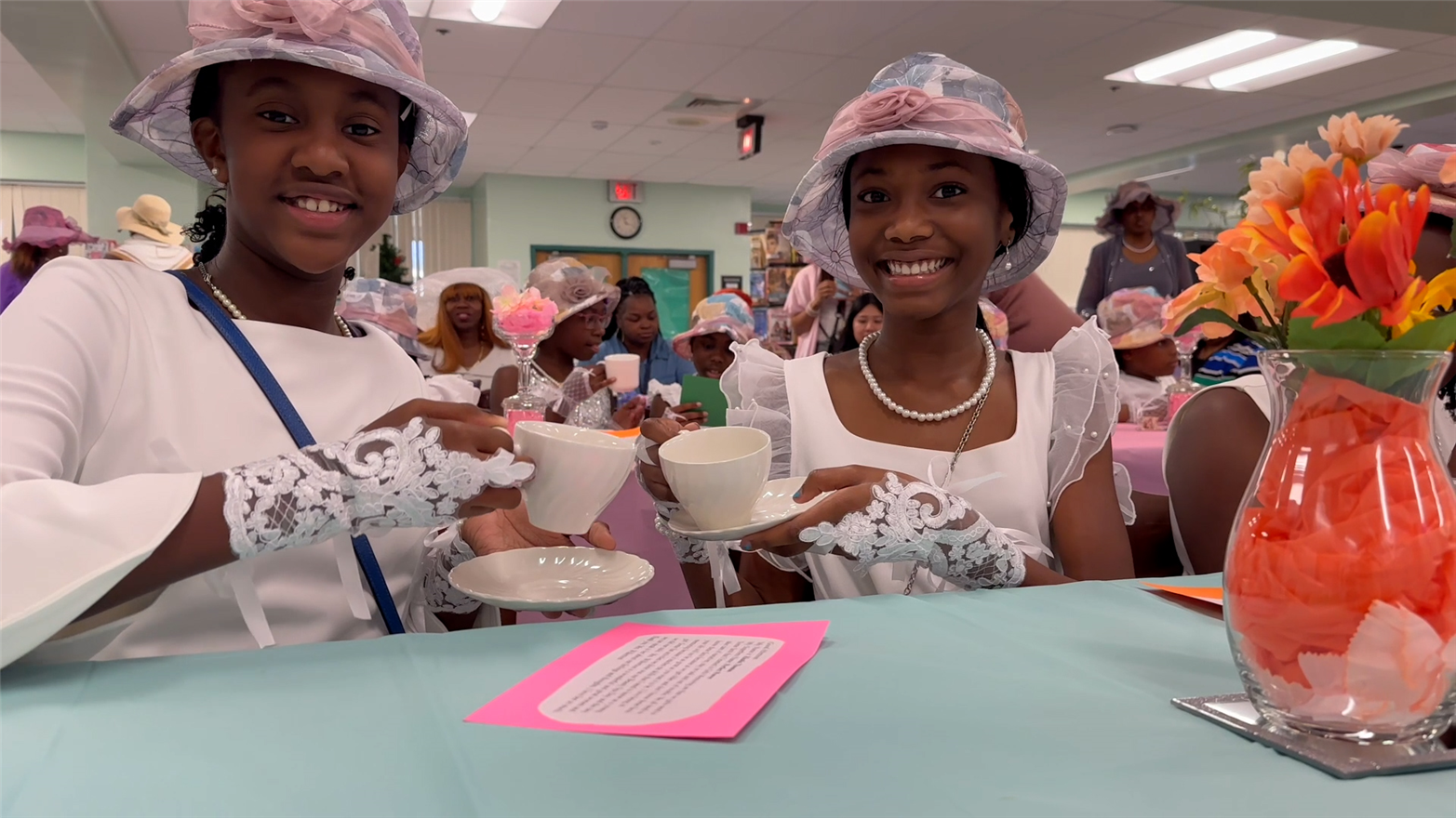 Two girls, holding teacups, in dresses and tea hats